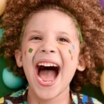 Menino sorridente com cabelos cacheados e pintura colorida no rosto