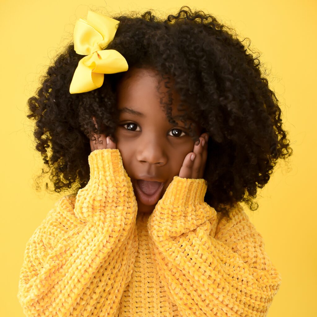 Menina com cabelos cacheados e laço amarelo usando suéter amarelo