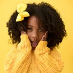 Menina com cabelos cacheados e laço amarelo usando suéter amarelo