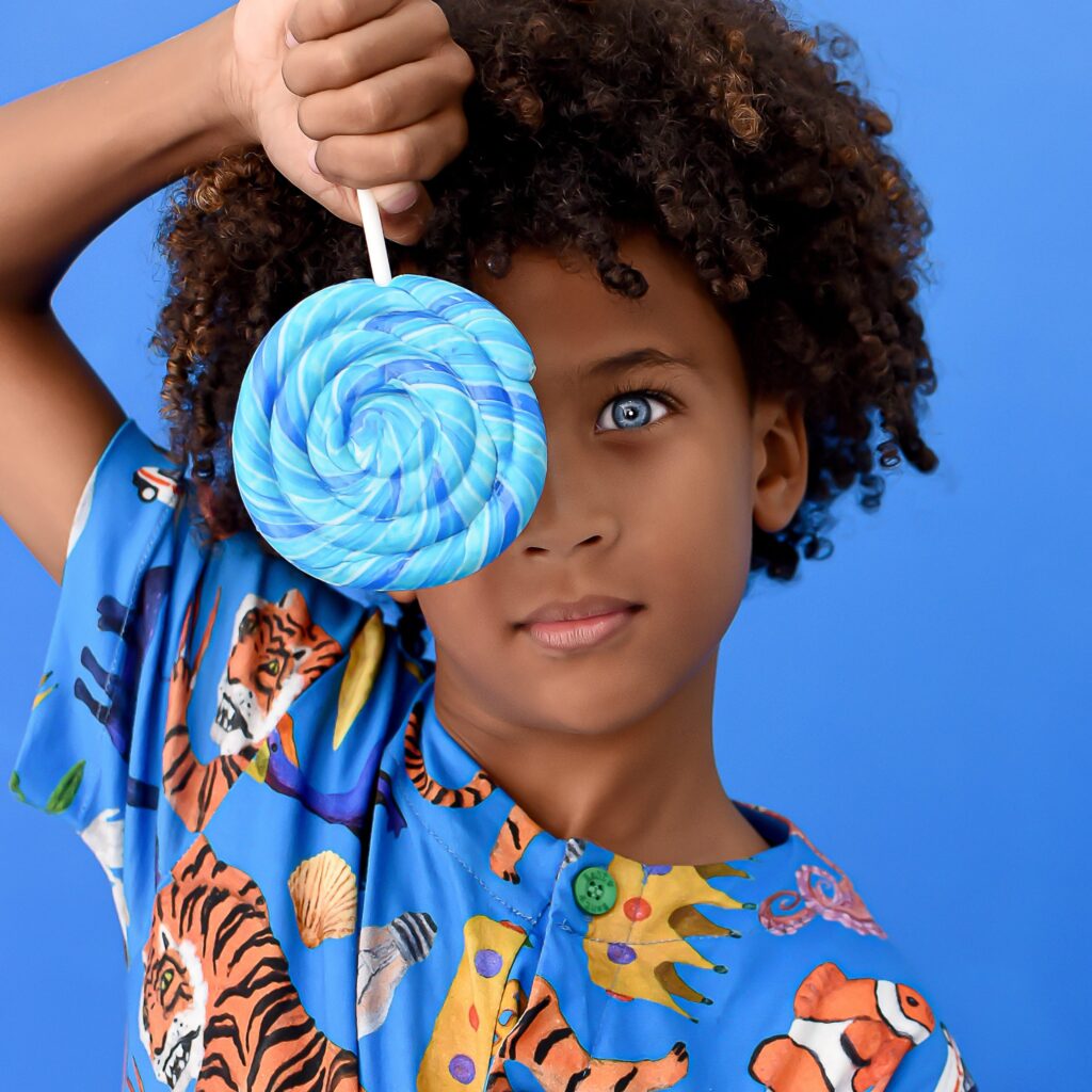Menino segurando pirulito azul em frente ao olho com camisa colorida