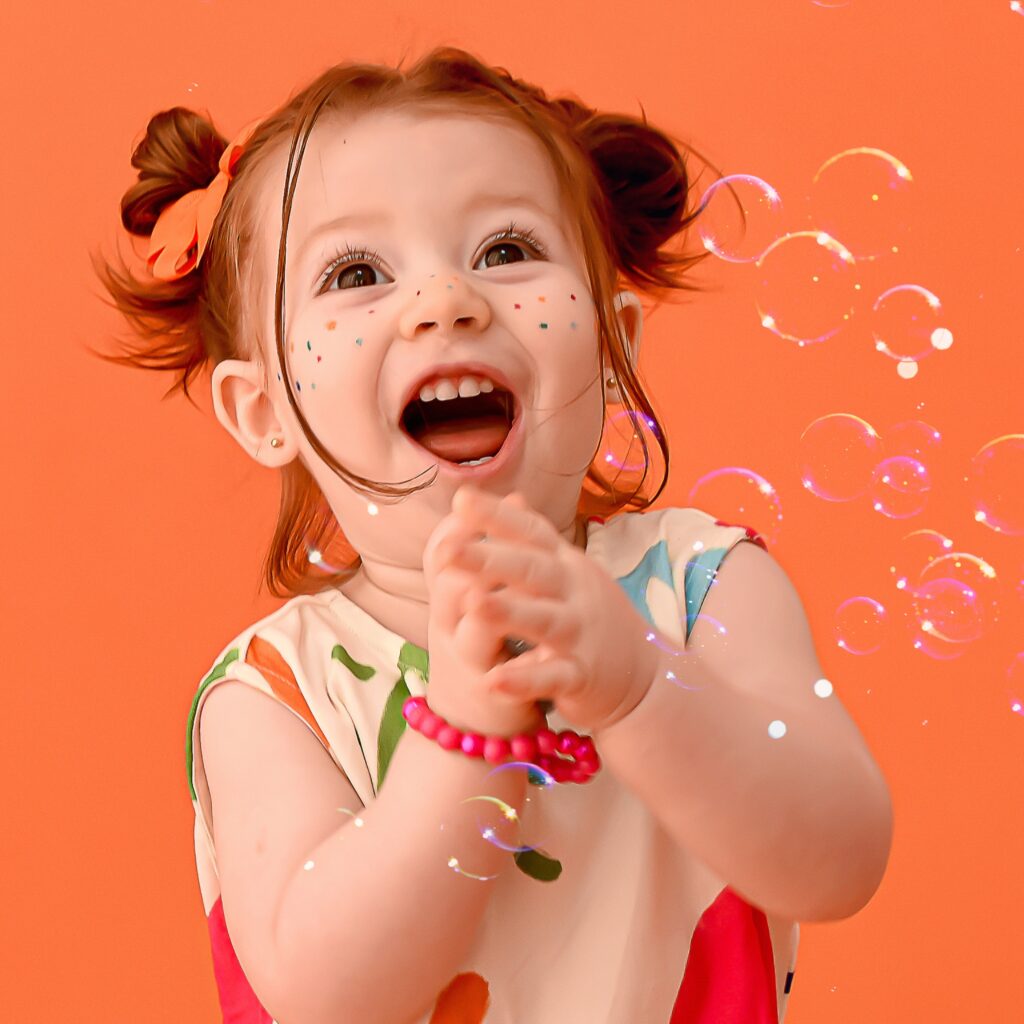 Menina sorridente brincando com bolhas de sabão em fundo laranja