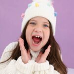 Menina sorridente com gorro branco de inverno em fundo lilás