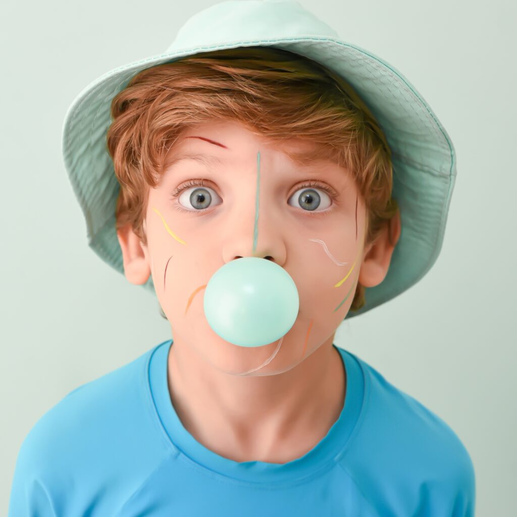 Menino com chapéu azul assoprando balão de chiclete em fundo claro